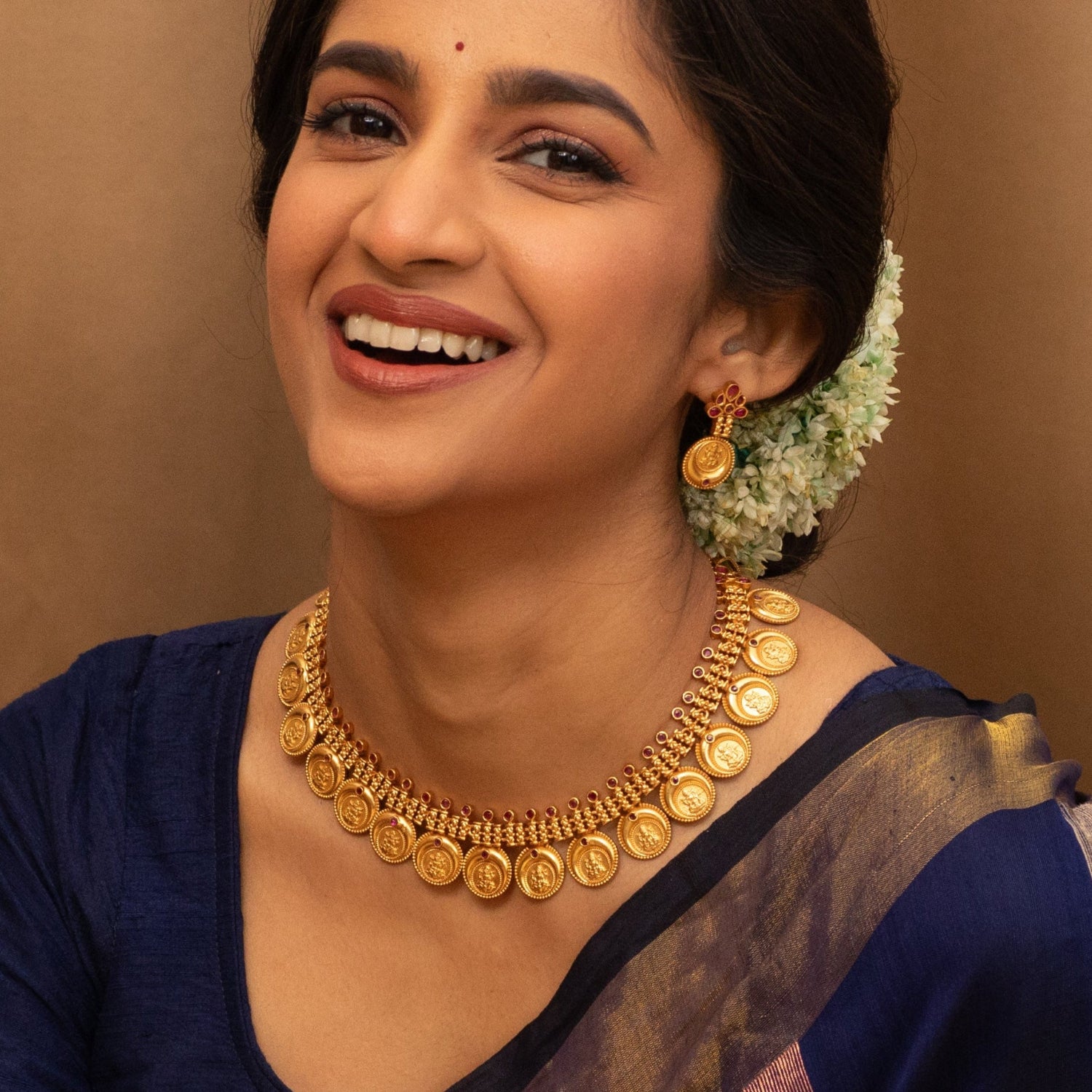 A picture of an Indian artificial gold plated necklace set with a round pendant and matching earrings, featuring intricate filigree work and red gemstones.