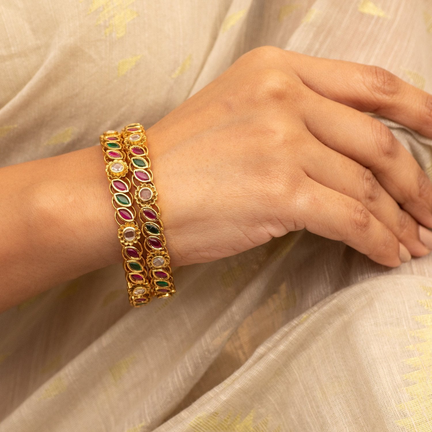 Close-up photo of a woman's hand holding a gold plated bangle with colorful gemstones.