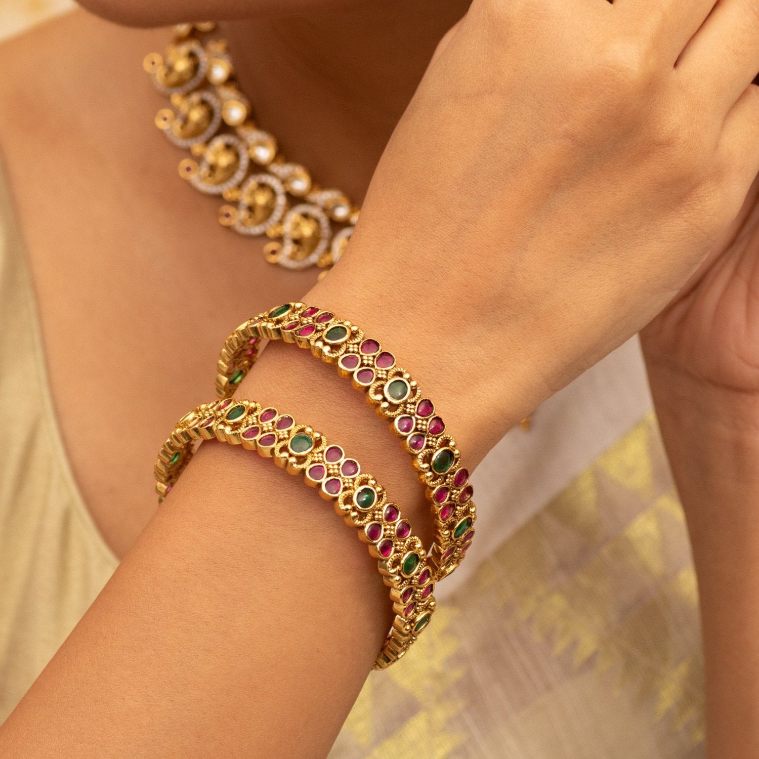 A close up image of a gold plated bracelet with green and red gemstones.